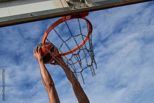 From below of African American male player jumping and scoring ball in basketball hoop during game on sports ground