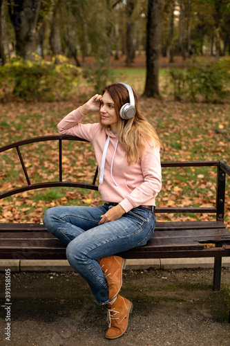 young beautiful happy smiling girl listening to music with headphones and drinking coffee in the autumn Park