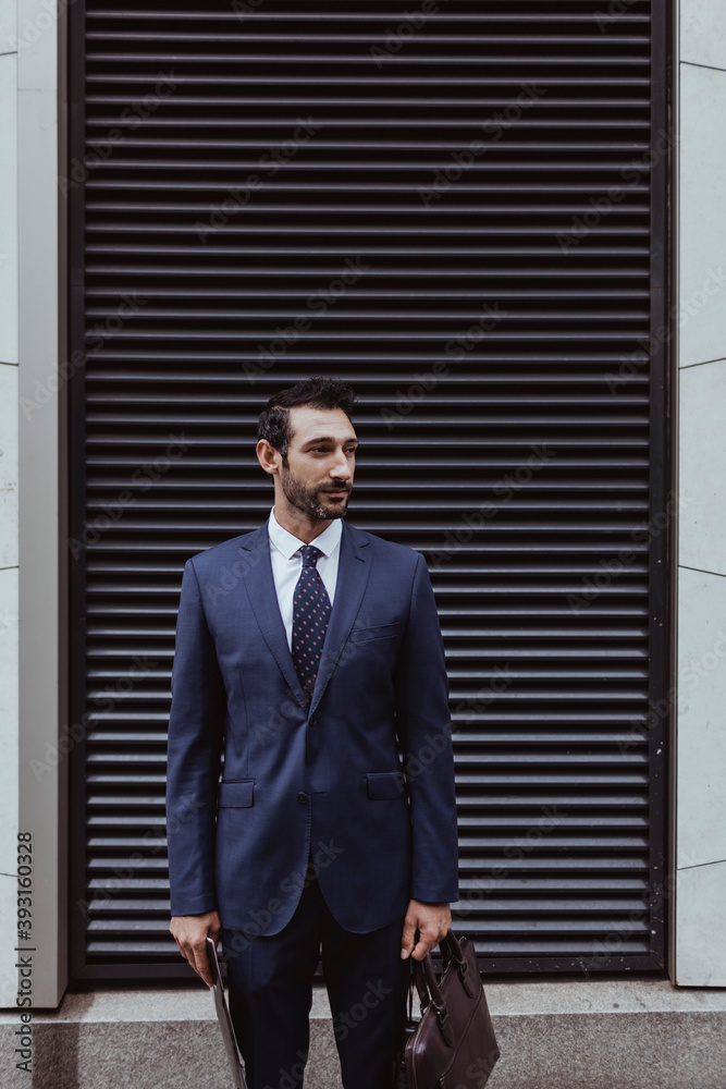 Smiling entrepreneur looking away while standing against shutter in city Smiling entrepreneur looking away while standing against shutter in city