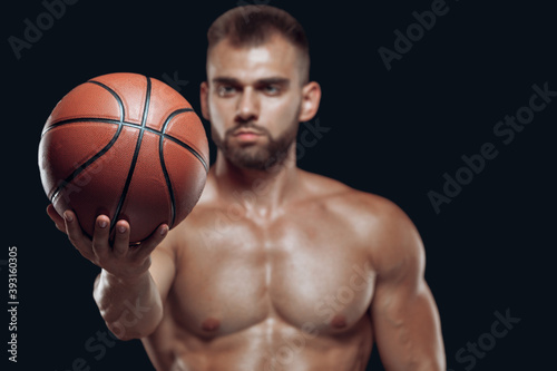 Close up of a basketball in a stretched hand of a muscular male player isolated on black background © satyrenko