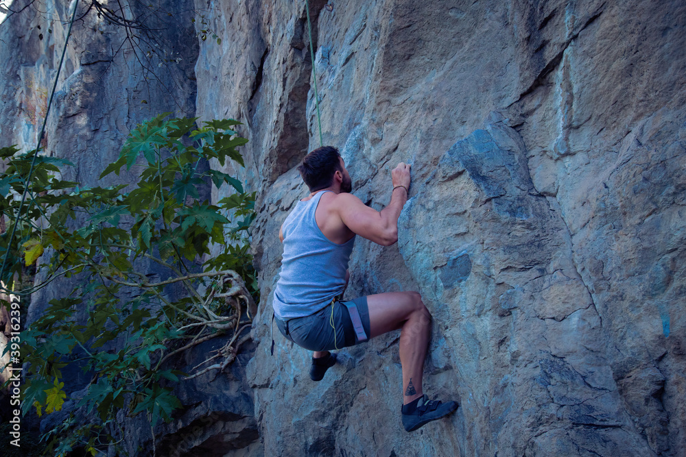 A young man with a rope engaged in the sports of rock climbing on the rock