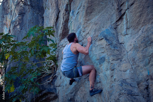 A young man with a rope engaged in the sports of rock climbing on the rock