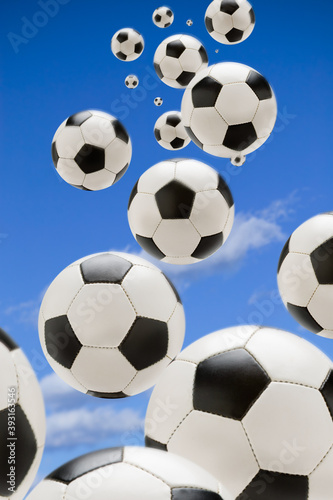 Many soccer balls fall through a blue sky toward viewer
