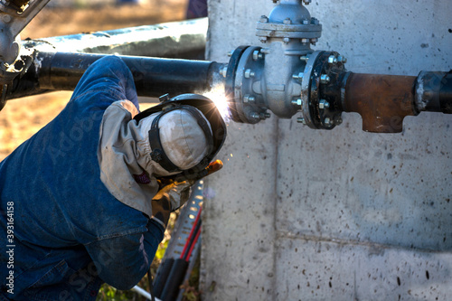 Welder welding metal pipes with protective mask in daylight and sparks.