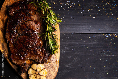 fried beef steak drizzled with butter lies on a wooden cutting board with rosemary, chili and garlic on a black background. flat lay. Horizontal photo. free space for advertising logotypes of inscript photo