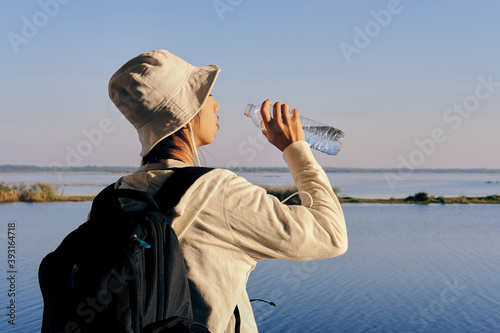 A person drinks water by a tranquil lake, enjoying a peaceful moment in nature.