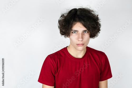 Teenage boy in a red T-shirt on a light background with an angry face because he has a headache because he quarreled with friends