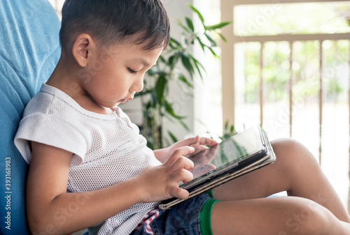 Little Asian Kid's using Digital Touchscreen Phone Tablet doing Online Study. photo