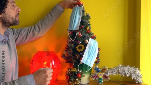 Europe, Italy , Milan - Man takes the mask from the Christmas tree - lifestyle at home during lockdown , Covid-19 Coronavirus quarantine  photo