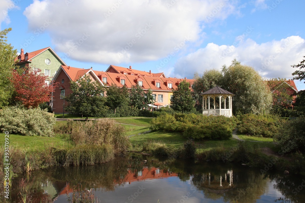 A view to a public park with a gazebo and a small pond. Behind the park, there are colorful residential buildings. These modern buildings are built on a traditional way. Scandinavian architecture.