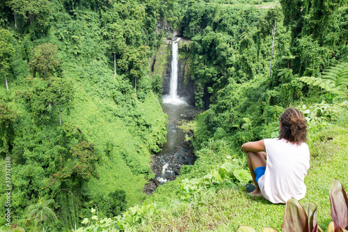 Male tourist with curly hair, looking at exotic Fuipsia waterfall photo