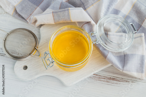 Homemade Ghee or clarified butter in a jar on white wooden table.