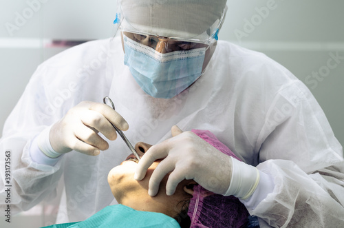 The dentist or doctor is wearing a white medical gown, mask and protective glasses in the background of the dentist's office