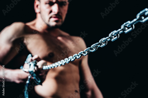 Muscular guy with chains on shoulders against a black background.