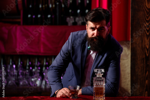 Barman luxury beverage concept. Man with beard holds glass with alcohol in bar. Waiter bartender in vintage vest with whiskey or scotch on tray.