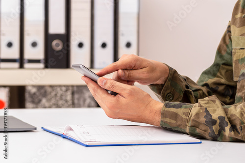 Closeup shot of an unrecognizable military man hands with agenda using phone at office photo