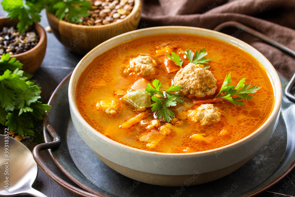 Soup close-up. Tomato-lentil soup with meatballs and vegetables on a dark slate table top. Soup close-up. Tomato-lentil soup with meatballs and vegetables on a dark slate table top.