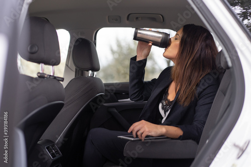 businesswoman dressed in jacket drinking tea in a car