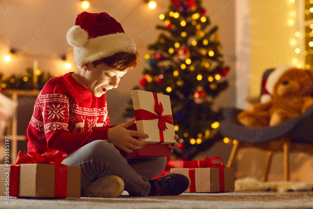 Cheerful boy feeling happy after opening festive gift box with Christmas presents inside Cheerful boy feeling happy after opening festive gift box with Christmas presents inside