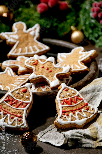 Homemade traditional Christmas gingerbread cookies with icing ornate. Gingerbread Man, angel, bell on ceramic plate with xmas decorations over dark background.