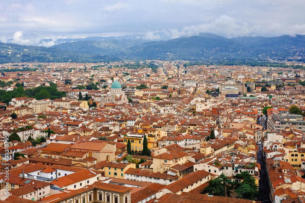 View of Florence and the mountains from the dome of the cathedral. Many houses with red roofs and a beautiful cathedral. There is fog over the mountains.