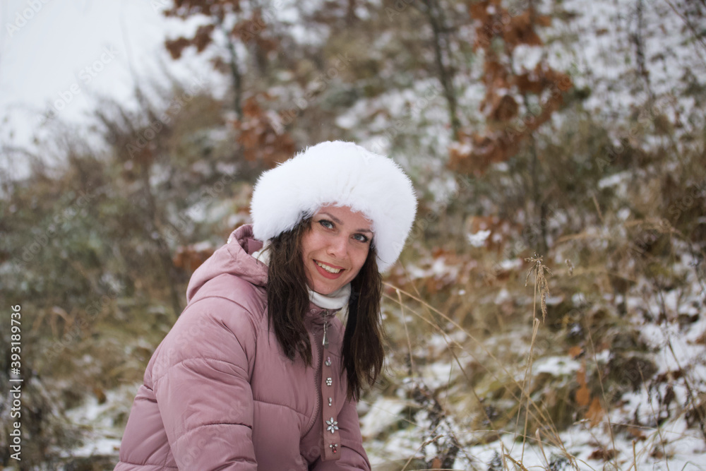 Portrait of a girl in a winter hat. Against the background of the ground covered with the first snow.