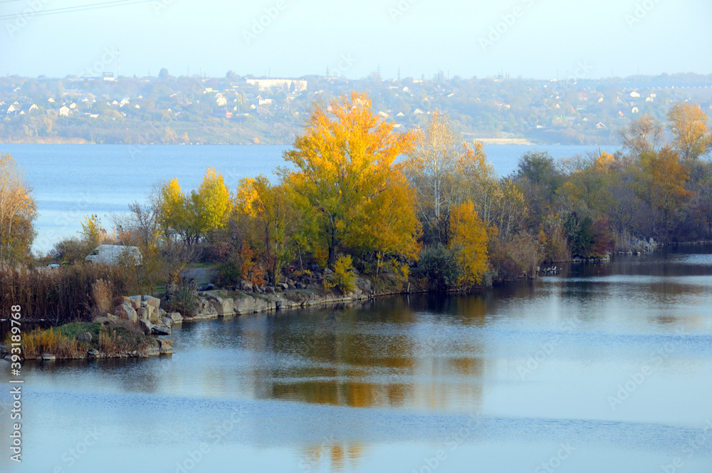 The river bank is covered with trees with yellow autumn foliage. Late autumn landscape on the river bank.