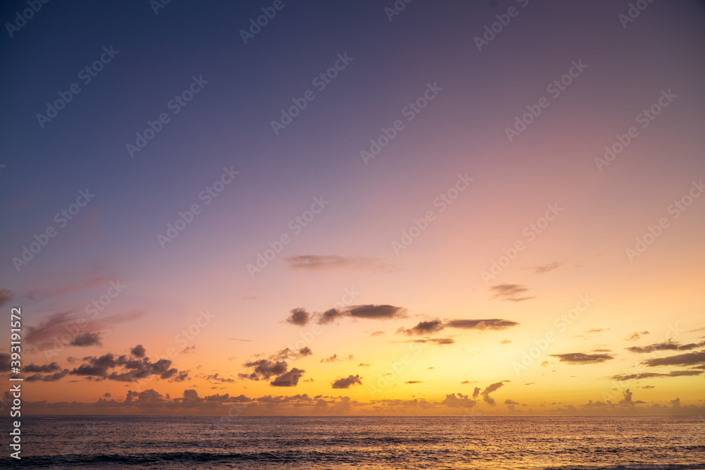 Dramatic sea shore sunset with sun setting down at the cloudy skyline with orange and vivid blues.
