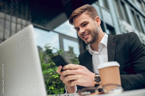 Handsome young businessman having coffee and texting