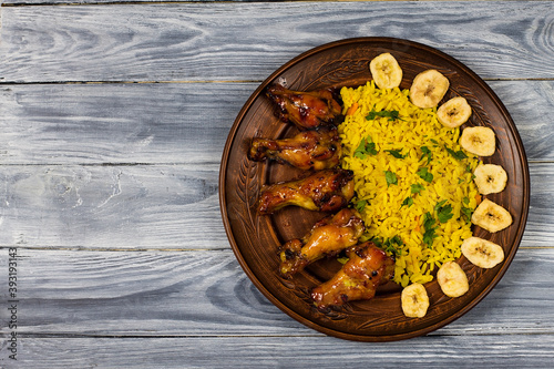 West African food. Rice with fried chicken and bananas, on a wooden background