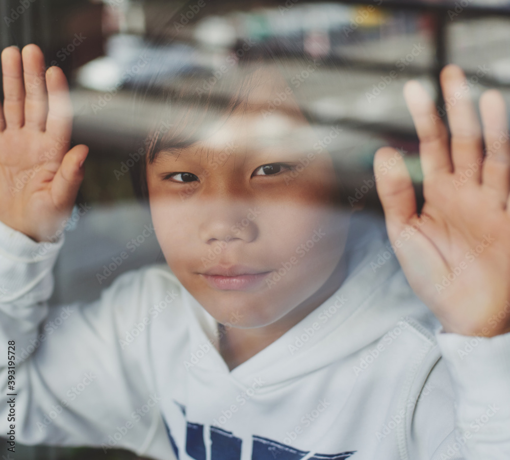 Niño asiático confinado en su hogar por el covid-19 mirando la calle a traves del cristal. - obrazy, fototapety, plakaty 