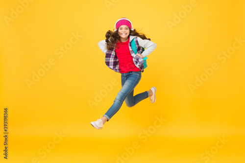 Active small kid run with travel bag listening to music in headphones yellow background, traveling