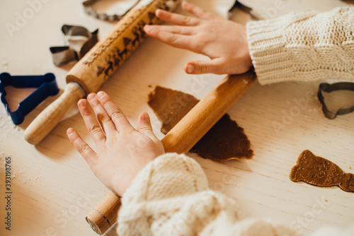 Top view of kid's hands making Christmas cookies or ginger bread in cozy kitchen with warm light