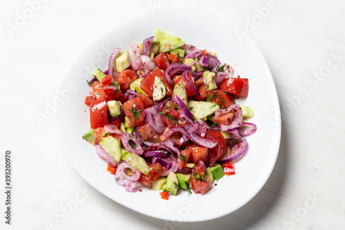 vegetable salad with red onion, tomato, cucumber, avocado, dill, sumach, paprika, olive oil in white bowl on wooden table