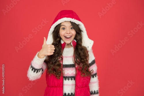 cheerful kid has beautiful hairstyle in warm winter clothing on new year holidays show thumb up  best offer