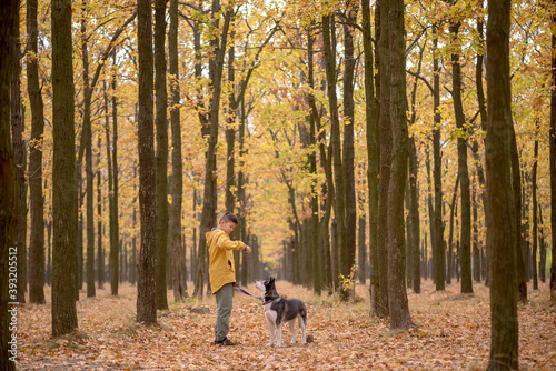 Handsome boy in a yellow raincoat with a husky dog in the forest