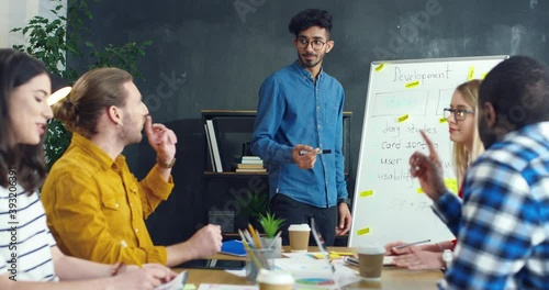 Hindu young man finishing his report on business startup strategy and colleagues applauding. Meeting of startuppers. Male sharing ideas on company development. photo