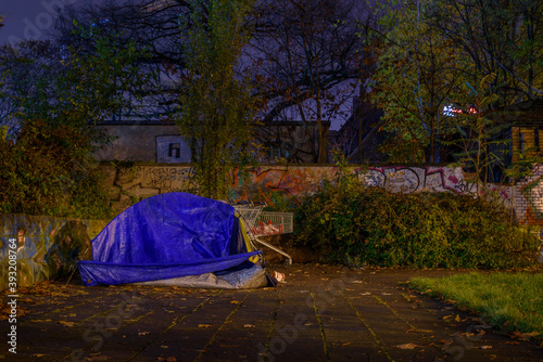 Fototapeta Naklejka Na Ścianę i Meble -  Tent of a homeless person in the city at night, shopping cart and a tent of a homeless person at night, rainy weather