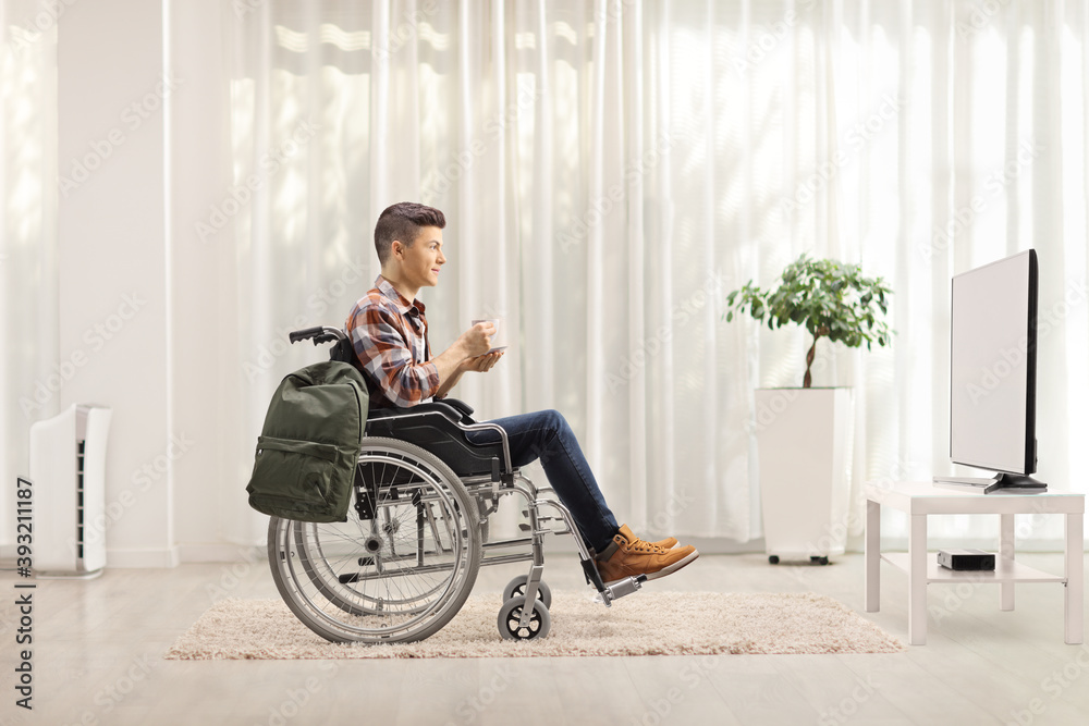Young man in a wheelchair with a cup of tea watching tv Young man in a wheelchair with a cup of tea watching tv