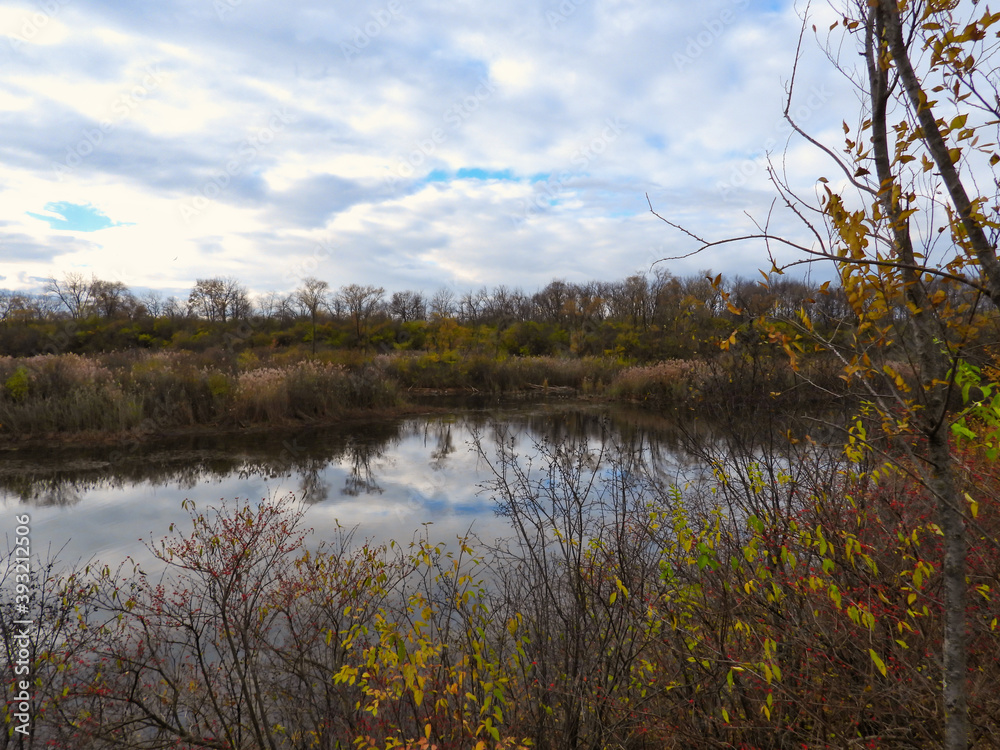 Lake in autumn: Looking across a like in late autumn under a beautiful sky with a lot of clouds but still showing some blue spots as reflected in the water surrounded by brown vegetation Lake in autumn: Looking across a like in late autumn under a beautiful sky with a lot of clouds but still showing some blue spots as reflected in the water surrounded by brown vegetation