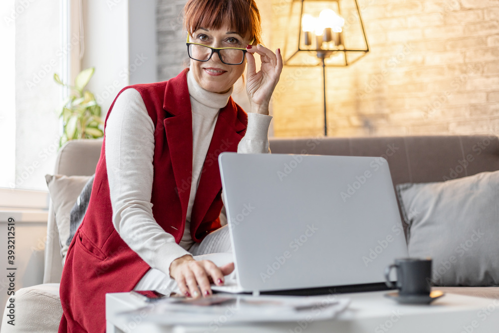 an adult woman with glasses sits on a sofa and works at a laptop at home an adult woman with glasses sits on a sofa and works at a laptop at home