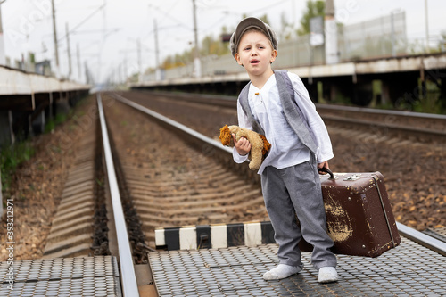 A little boy sitting on a suitcase cries and hugs his favorite toy. His train has left. Retro style clothing.