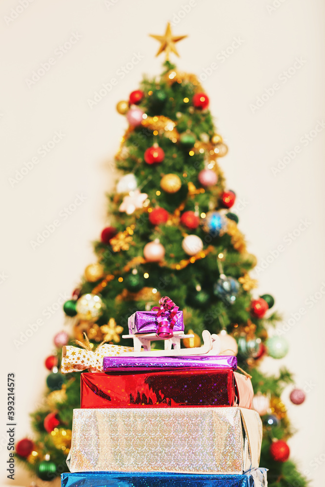 Packed gifts in front of colorful Christmas tree, winter holidays