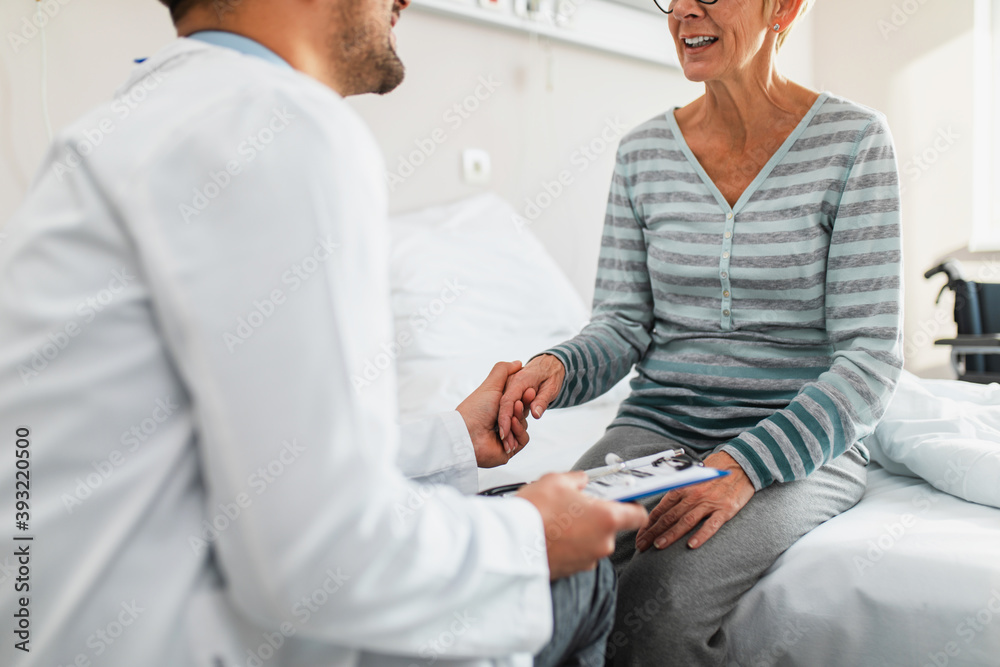 Obraz premium Young doctor visiting sick senior woman in hospital room or nursing center.