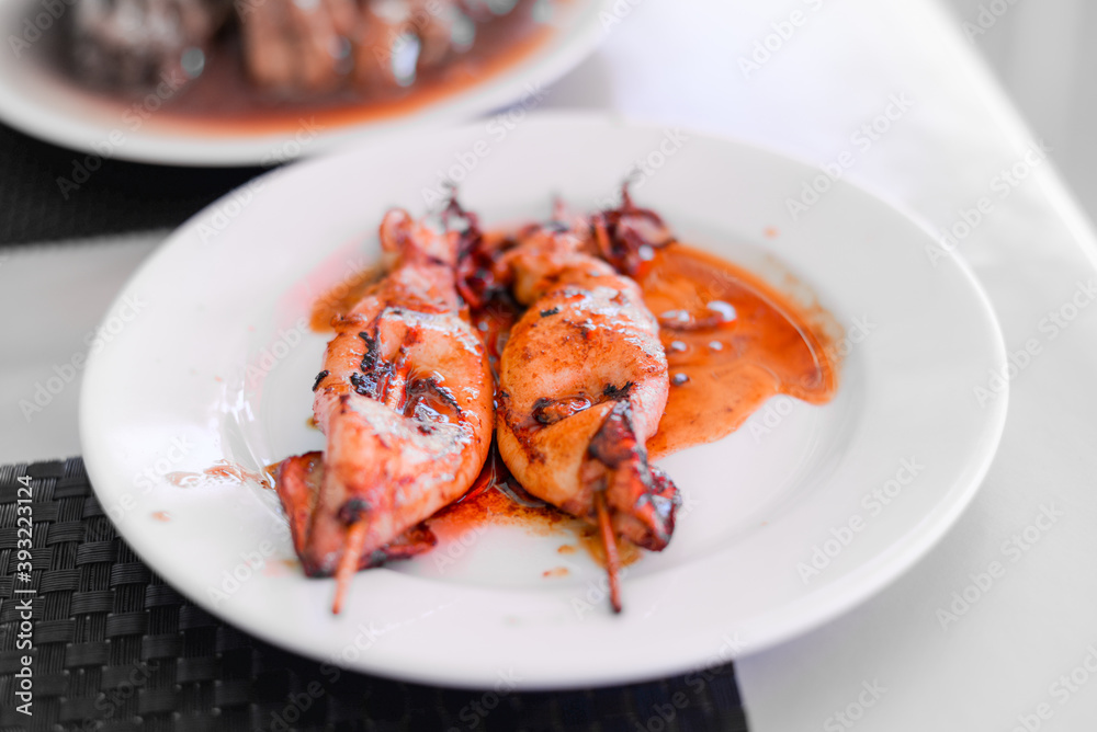 Grilled Squids on wooden sticks on white plate in spicy sause. A dish of Chinese cuisine. Grilled Squids on wooden sticks on white plate in spicy sause. A dish of Chinese cuisine.