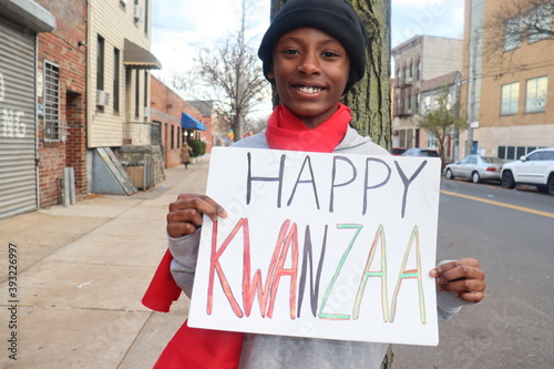 Black kid holding Happy Kwanzaa sign outdoors on city street