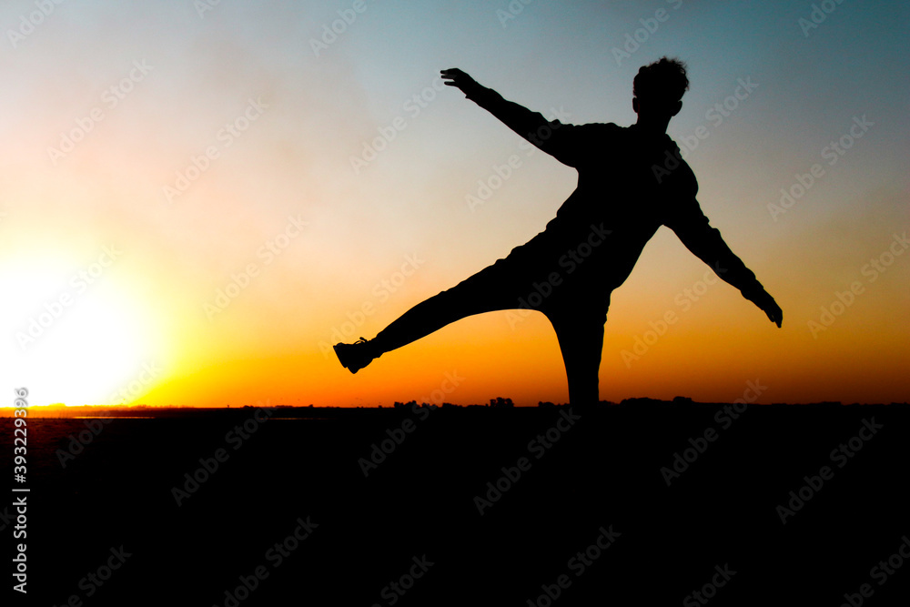 silueta de chico al atardecer haciendo equilibrio en un pie a contraluz silueta de chico al atardecer haciendo equilibrio en un pie a contraluz