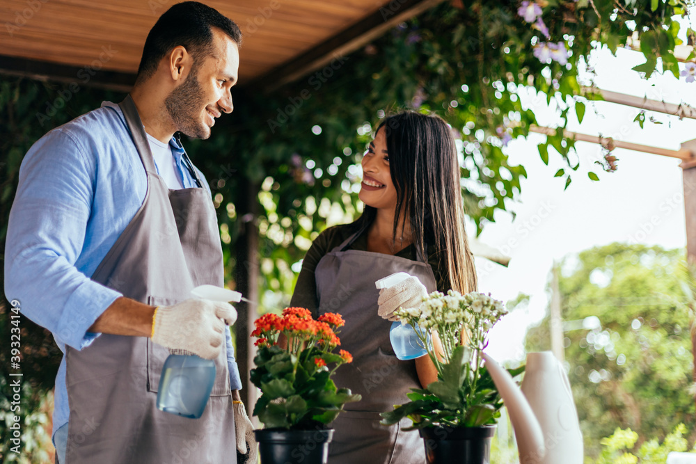 Latin wife and husband watering potted plants at home