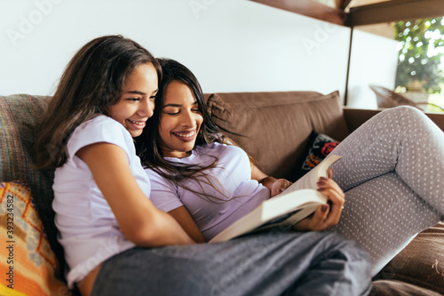 Latin mother and daughter reading a book together on the couch in the morning