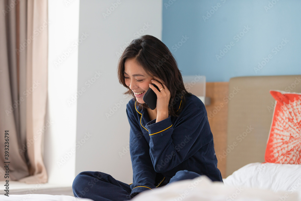 happy young asian woman sitting in bed talking on mobile phone indoor at home happy young asian woman sitting in bed talking on mobile phone indoor at home